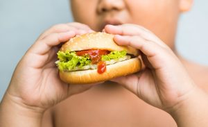 criança comendo hamburguer e ressaltando a importância da atividade física no combate a obesidade infantil