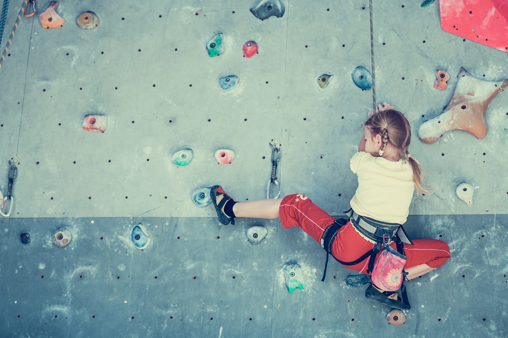 garotinha que pratica atividade física para crianças como parede de escalada